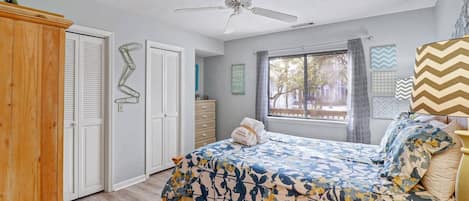 Un dormitorio con una cama, un ventilador de techo, una ventana con cortinas y un armario de madera.