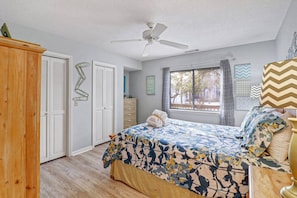 A bedroom with a bed, a ceiling fan, a window with curtains, and a wooden wardrobe.