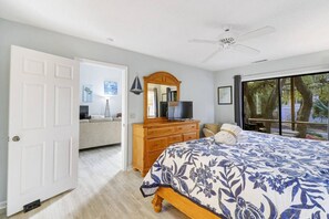 A bedroom with a bed, a dresser, a television, and a large window with a view of trees.