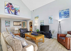 A spacious living room with a sofa, a coffee table, a television, and artwork on the walls.