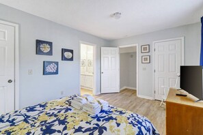 Une chambre à coucher avec un lit, une commode et un téléviseur. Des portes donnent accès aux autres pièces.