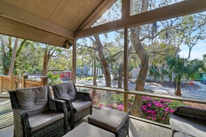 A covered outdoor seating area with wicker furniture and a view of trees and a parking lot. - 76 Dune Lane | Walk to Beach | Dog Friendly (Hilton Head Island)