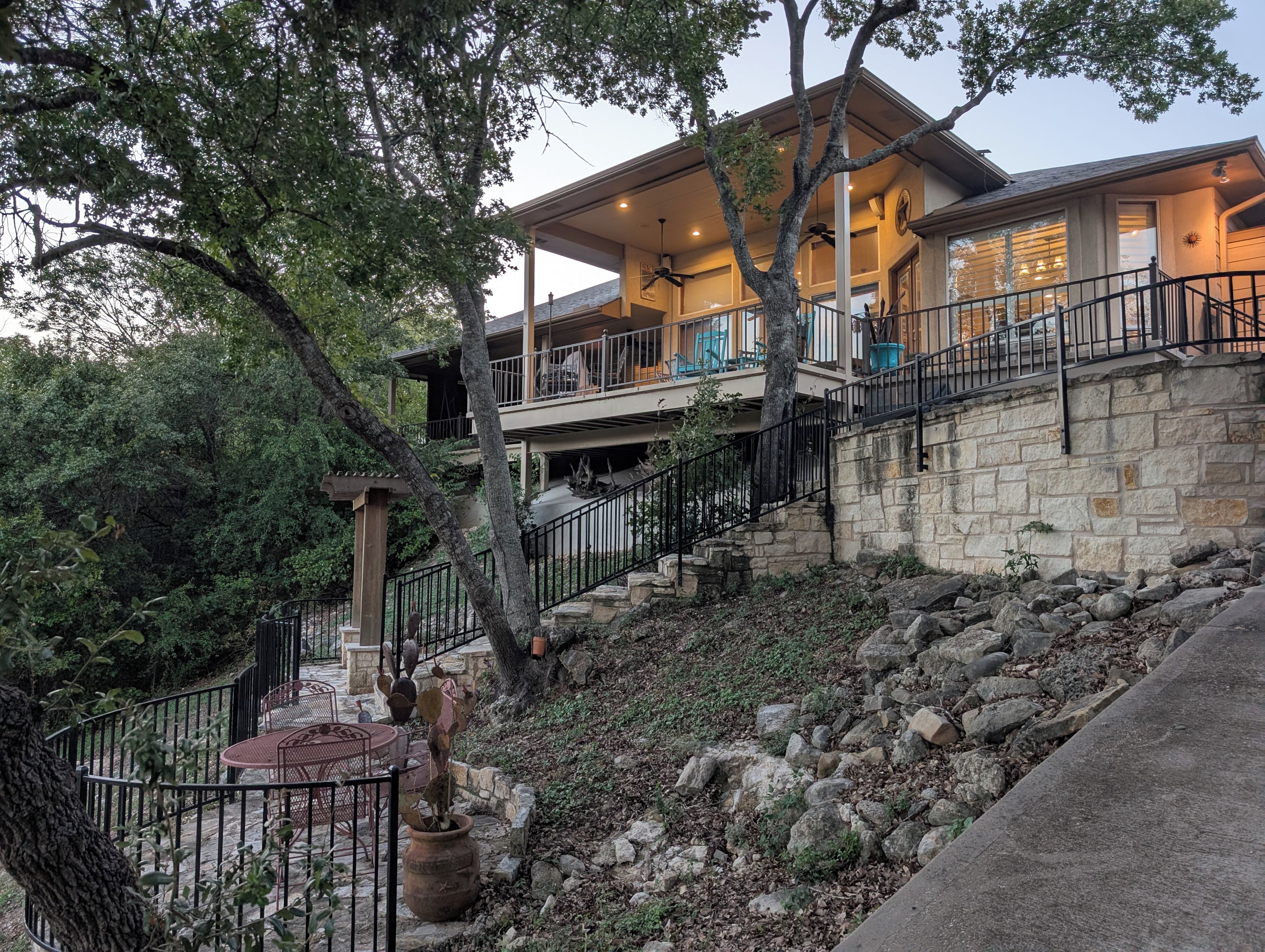 A two-story house with a stone exterior, a balcony with outdoor seating, and a staircase leading to the upper level.