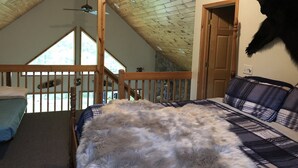 A bedroom with a wooden ceiling, a bed with a fluffy white cover, a plaid-patterned headboard, and a window with a view of trees. - Snowmobile, Skiing, and Outdoor Paradise/Cabin (Niagara)