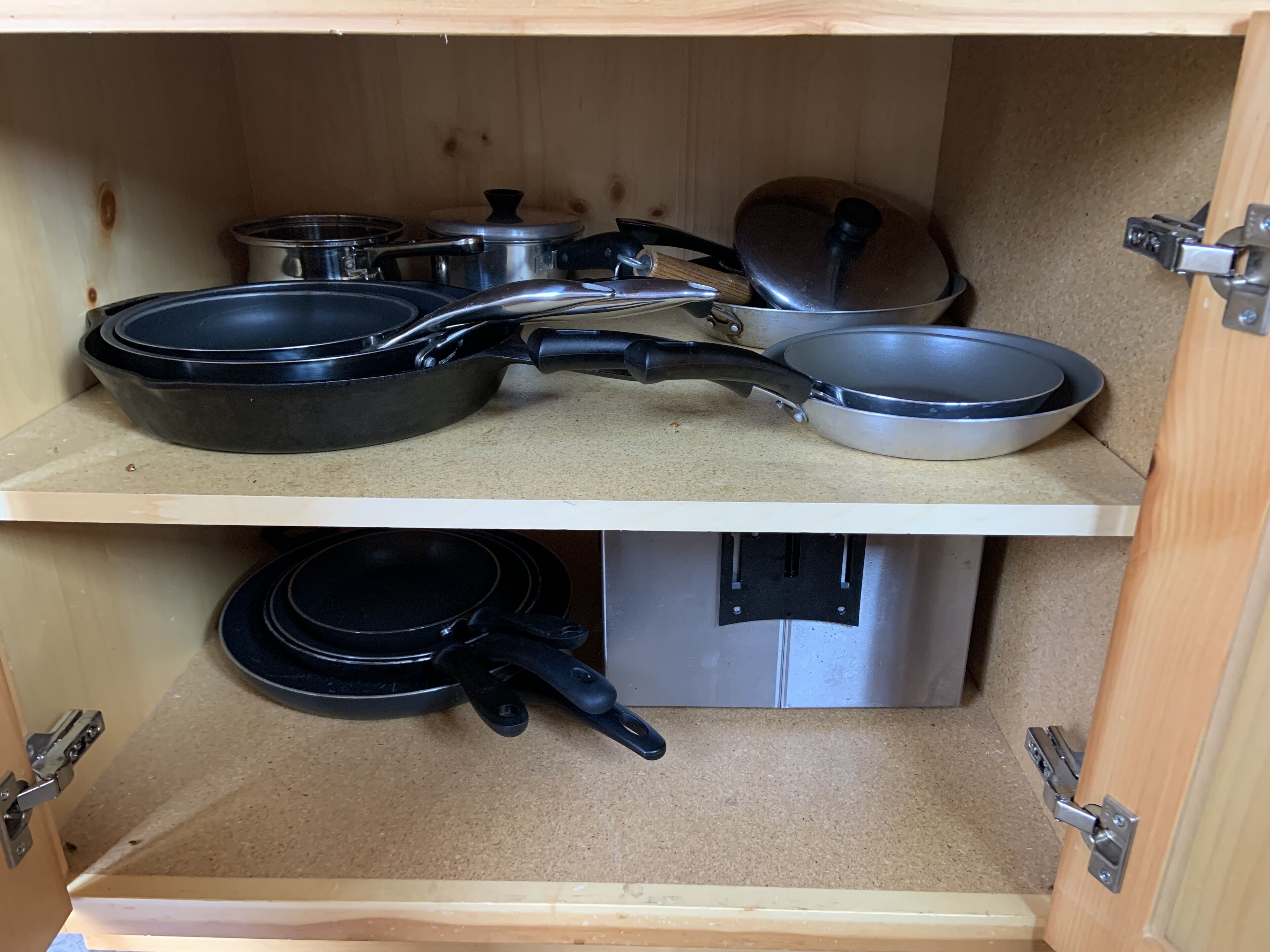 Eine Küchenschrank mit verschiedenen Kochutensilien, darunter Pfannen und Töpfen.