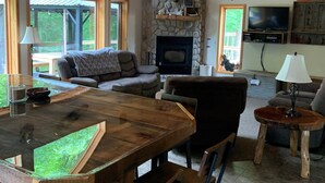 A rustic interior with a stone fireplace, wooden ceiling, and large windows offering views of greenery. - Snowmobile, Skiing, and Outdoor Paradise/Cabin (Niagara)