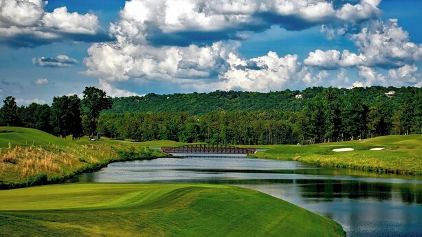 A golf course with a bridge over a pond, surrounded by lush greenery and trees. - Snowmobile, Skiing, and Outdoor Paradise/Cabin (Niagara)