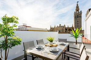 An outdoor dining area with a table set for four, surrounded by chairs, a potted plant, and a view of a historic building in the background. - Genteel Home Mateos Gago V (Seville)