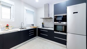 Une cuisine moderne avec des meubles noirs, des appareils en acier inoxydable et une fenêtre équipée de stores.
