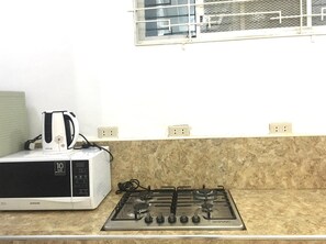 A kitchen with a microwave and gas stove. - Vitasolo Hometel & Suite (Tagum)