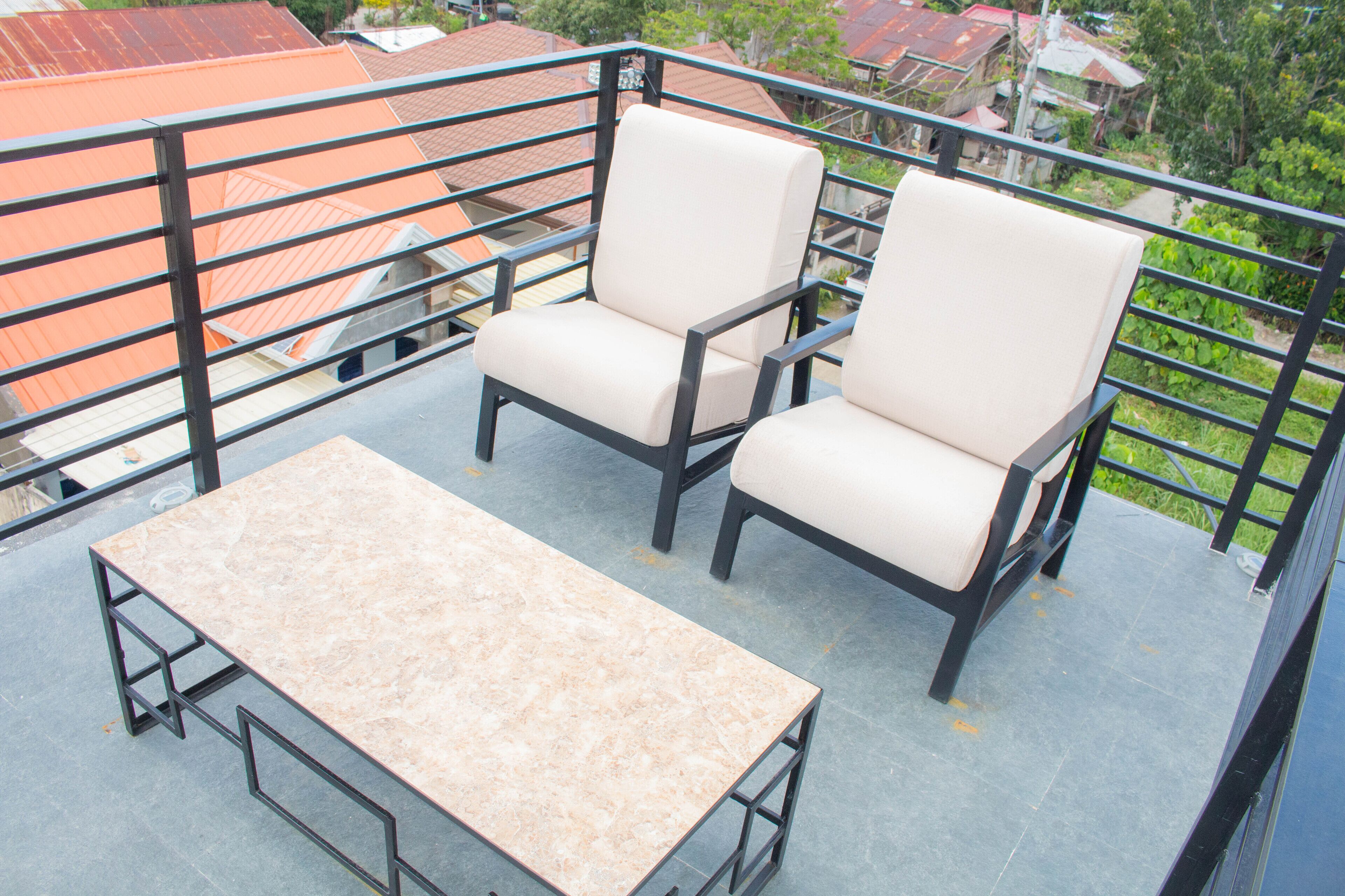 Ein Balkon mit zwei Stühlen und einem Tisch, mit Blick auf ein Wohngebiet mit roten Dächern.