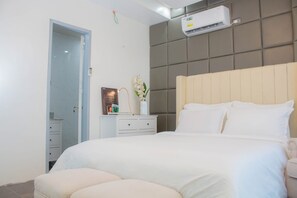 A bedroom with a large bed, a bedside table with a mirror, a wall-mounted air conditioner, and a door leading to another room. - Vitasolo Hometel & Suite (Tagum)