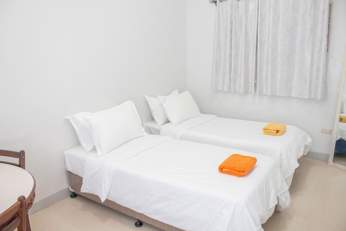 Quarto de hotel com duas camas de solteiro, uma cadeira de madeira e uma mesa pequena.