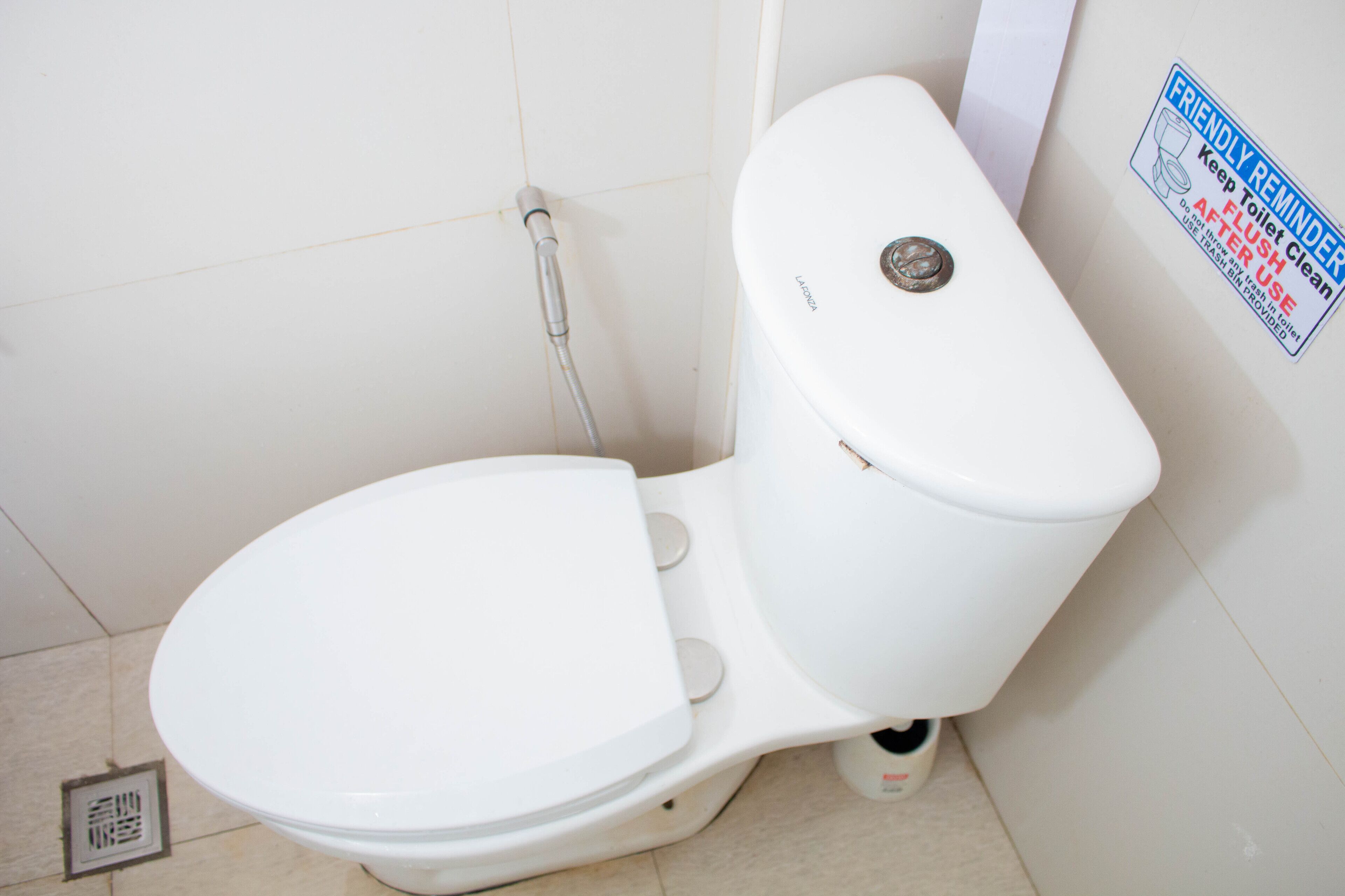 A white toilet with a flush handle and a sticker on the wall.