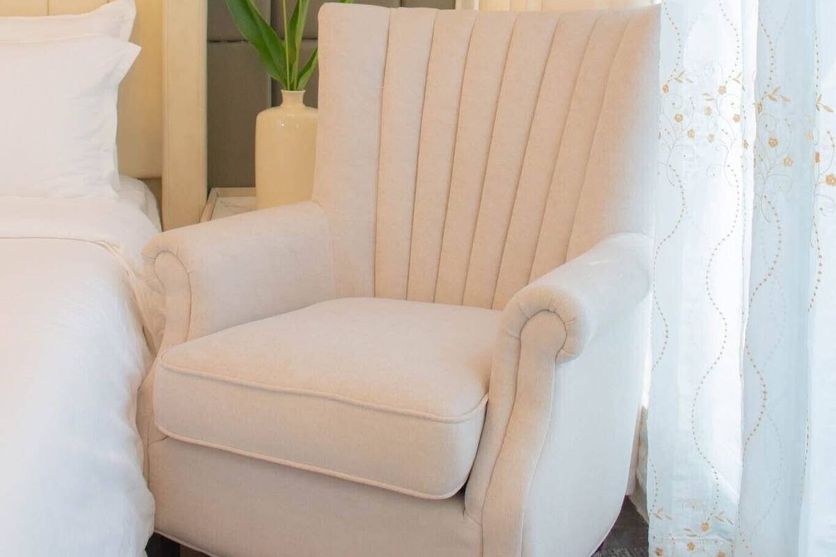 Quarto de hotel com uma cama, uma cadeira, um vaso com flores e um termostato fixado na parede.