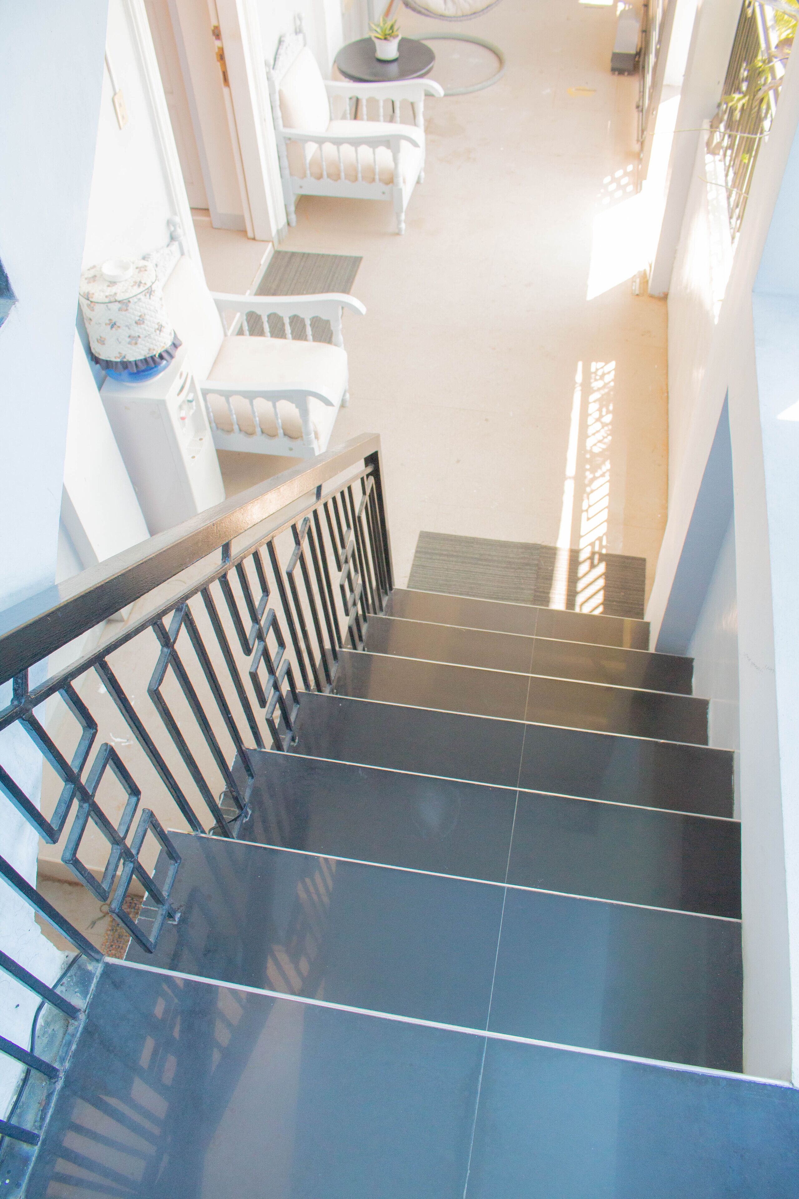 A staircase with black steps and a metal railing, leading to a room with a white chair and a small table with a plant.