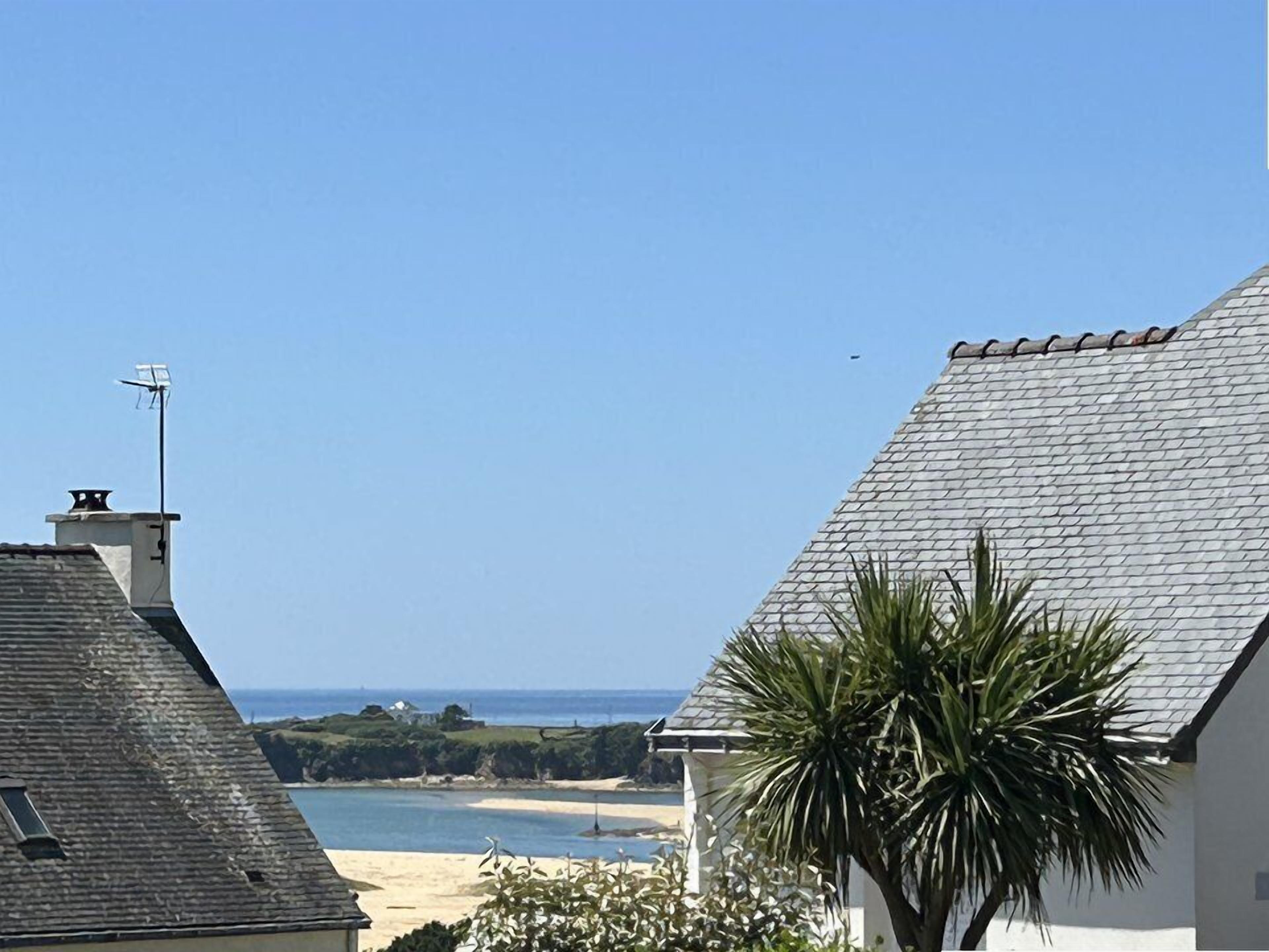 Vista costera con playa, un edificio blanco de techo a dos aguas y una palmera.