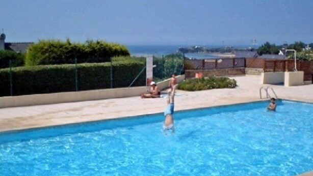 Una piscina amb aigua cristal·lina blava, un nen jugant i el mar de fons.