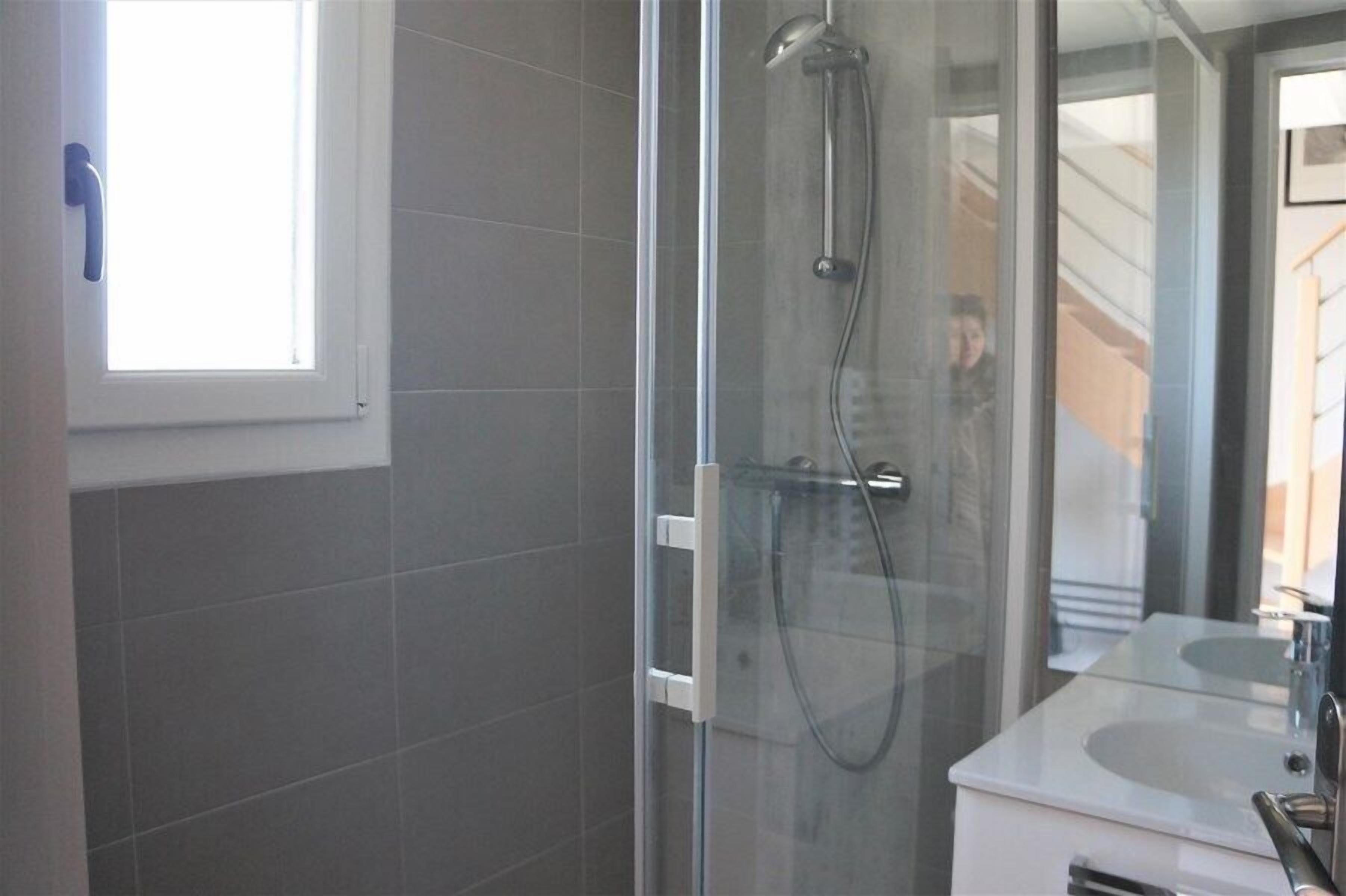 Un baño moderno con cabina de ducha de vidrio, un lavabo blanco y un espejo grande.
