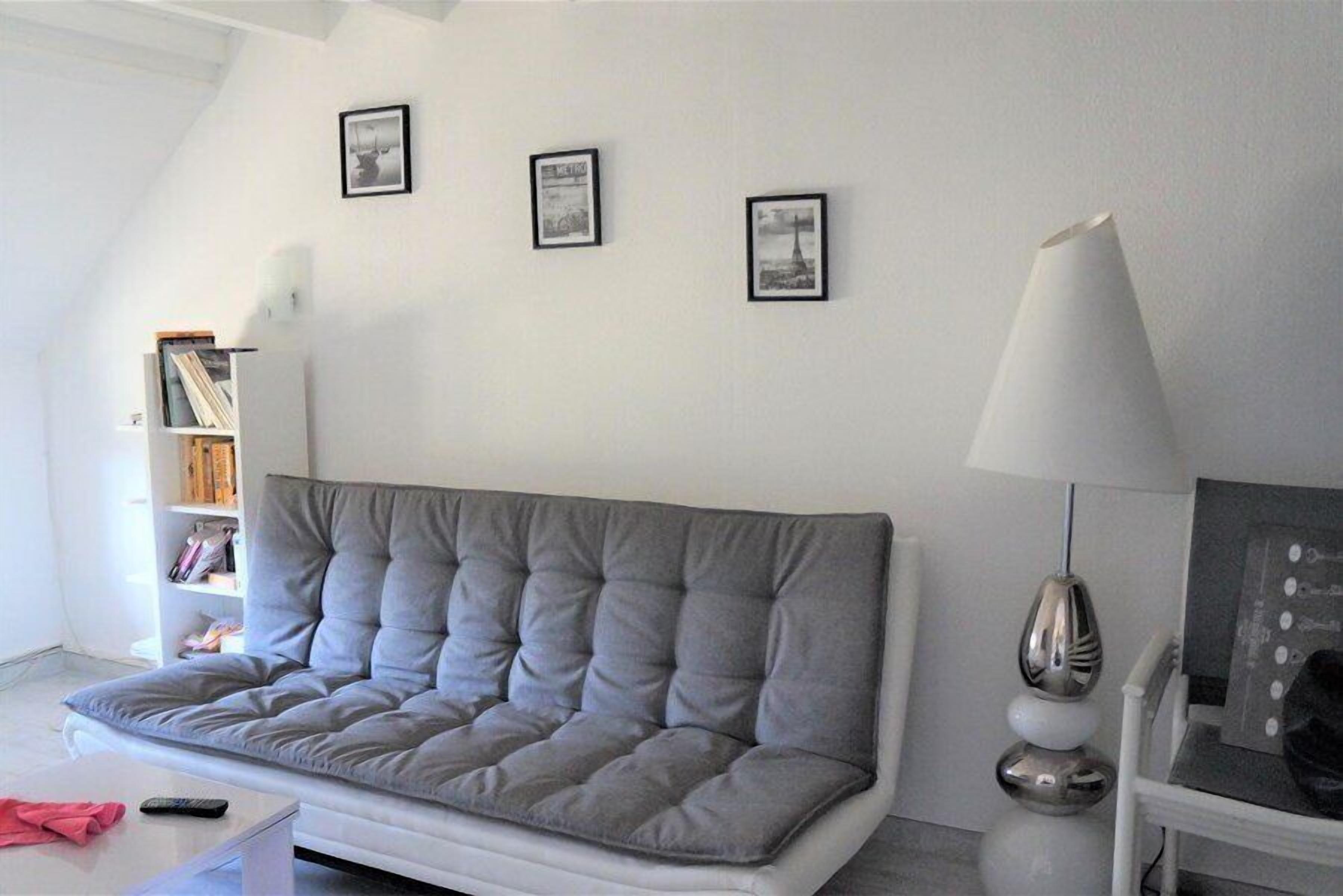 Een moderne woonkamer met een grijze bank, een witte bijzettafel, een lamp en een boekenkast.