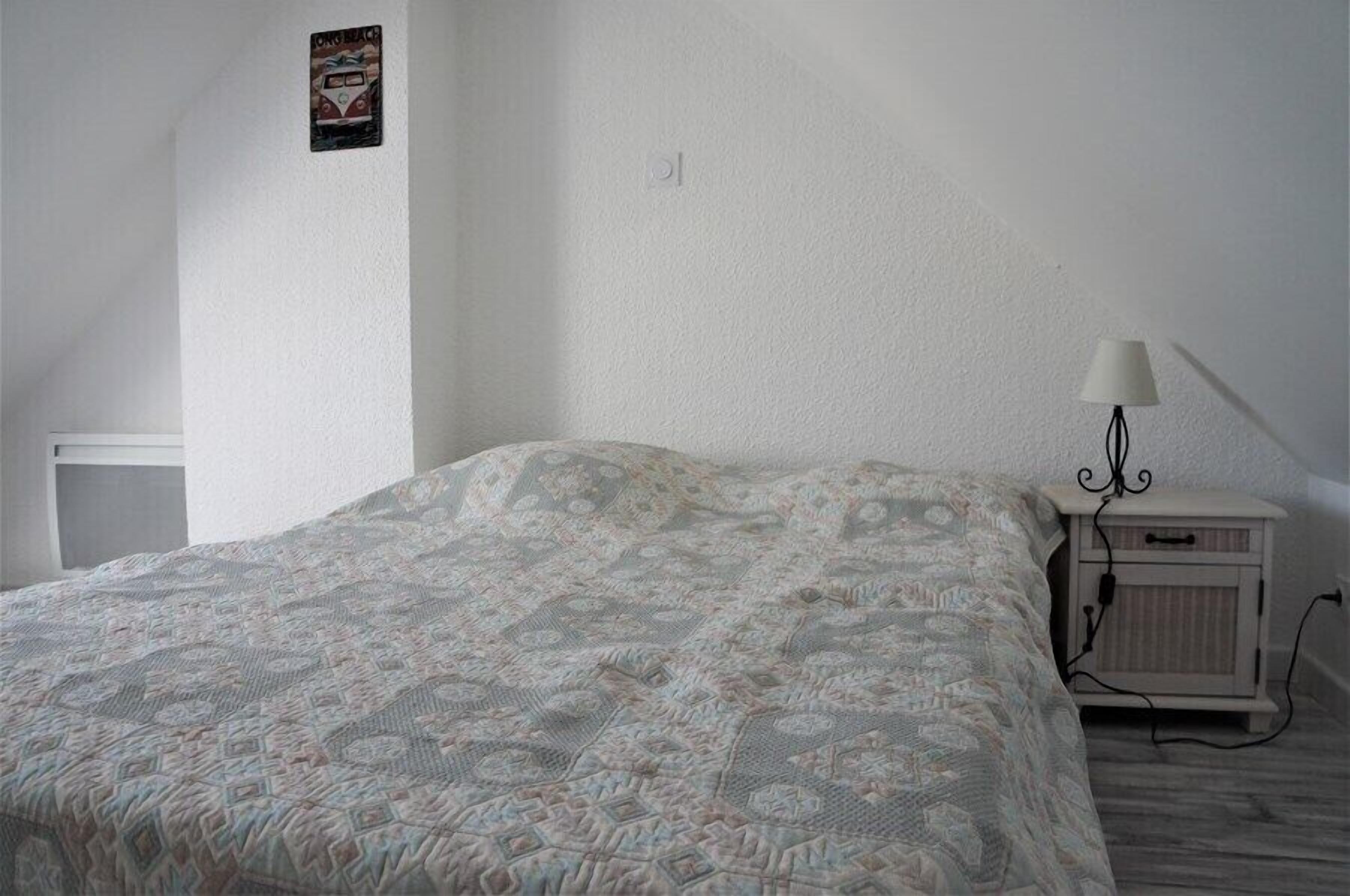 A bedroom with a patterned bedspread, a bedside lamp, and a small nightstand.