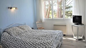 A bedroom with a bed, a chair, a TV on a stand, and a window with curtains.