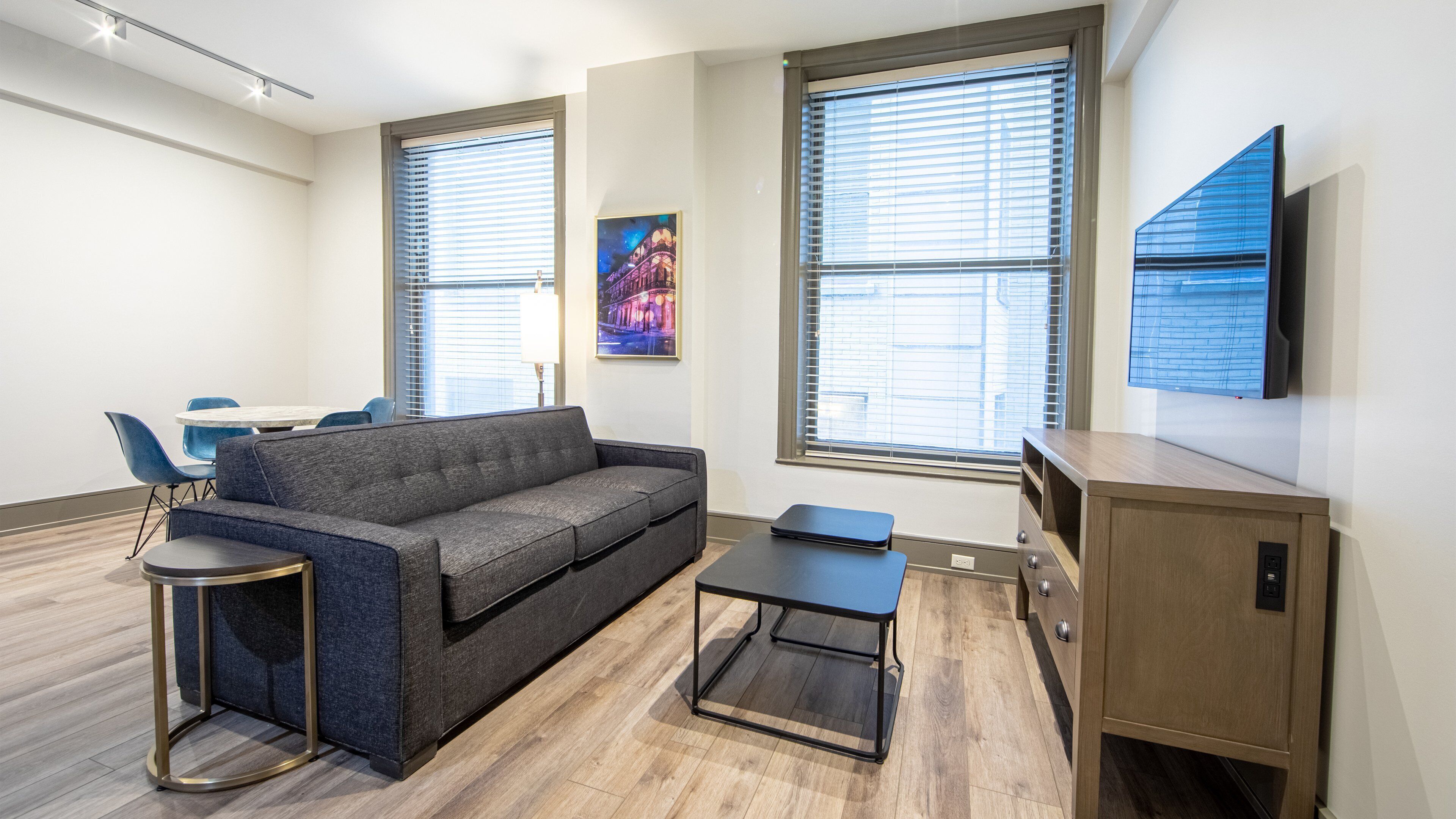 A modern living room with a grey sofa, a small round table, a cabinet, and a TV mounted on the wall.