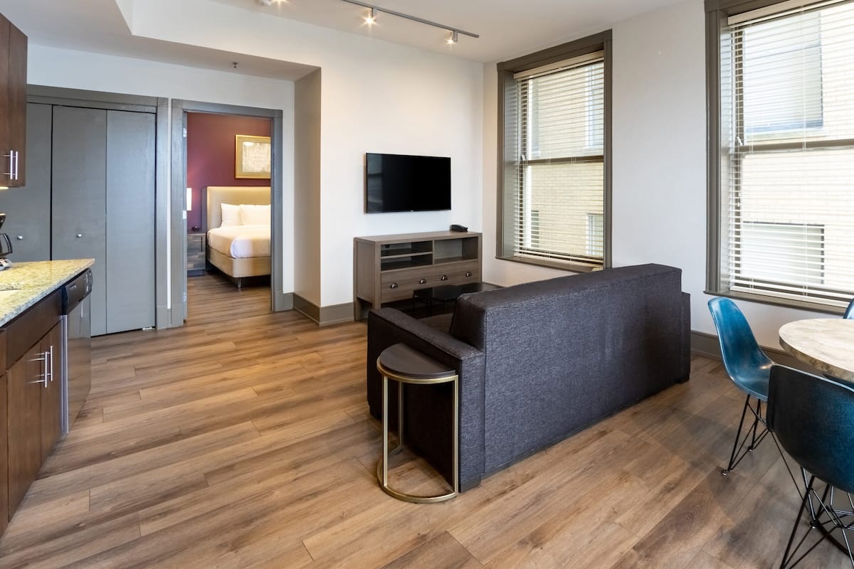 Un appartement moderne comprenant une cuisine, un espace de vie avec un canapé et une télévision, un coin repas avec une table et des chaises, et une chambre avec un lit et une table de chevet.