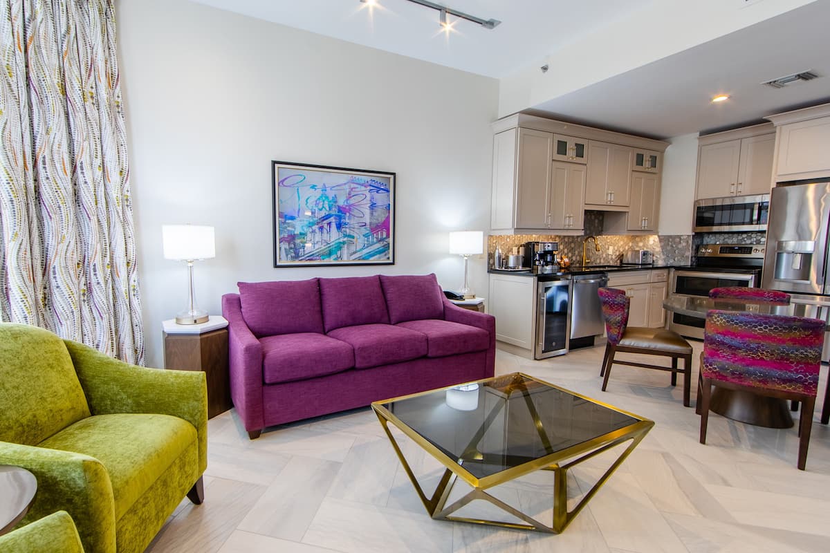 Un salon moderne avec un fauteuil vert, un canapé violet et une table basse en verre.