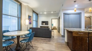 Moderni hotellihuone, jossa on ruokailutila, sohva, televisio ja pieni keittiö.