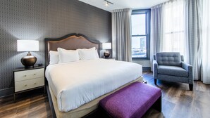 Moderni hotellihuone, jossa on suuri sänky, yöpöytä lampun kanssa, tuoli ja ikkuna, jossa on verhot.