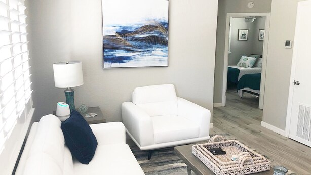Una sala de estar moderna con un sofá blanco, un sillón blanco, una mesa de centro y un cuadro en la pared.