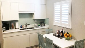 Cocina compacta con armarios blancos, un lavamanos y una zona de comedor con mesa y sillas.