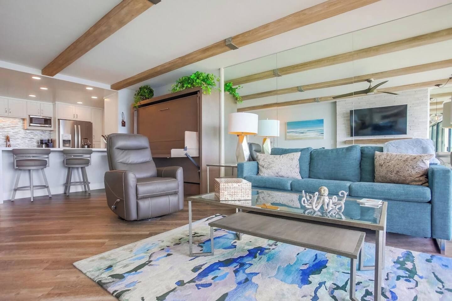 A modern living room with a sofa, a leather chair, a coffee table, and a kitchen area in the background.