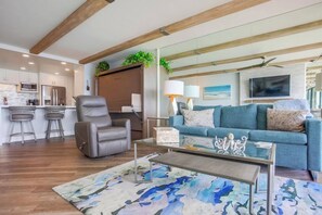 A modern living room with a sofa, a leather chair, a coffee table, and a kitchen area in the background.