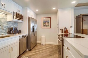 A modern kitchen with stainless steel appliances, a coffee maker, and a trash bin.