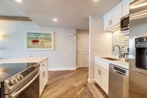 A modern kitchen with stainless steel appliances, a wooden floor, and a painting on the wall.