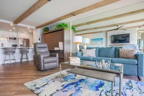Una sala de estar moderna con un sofá, un sillón reclinable, una mesa de centro y una zona de cocina con taburetes de bar.