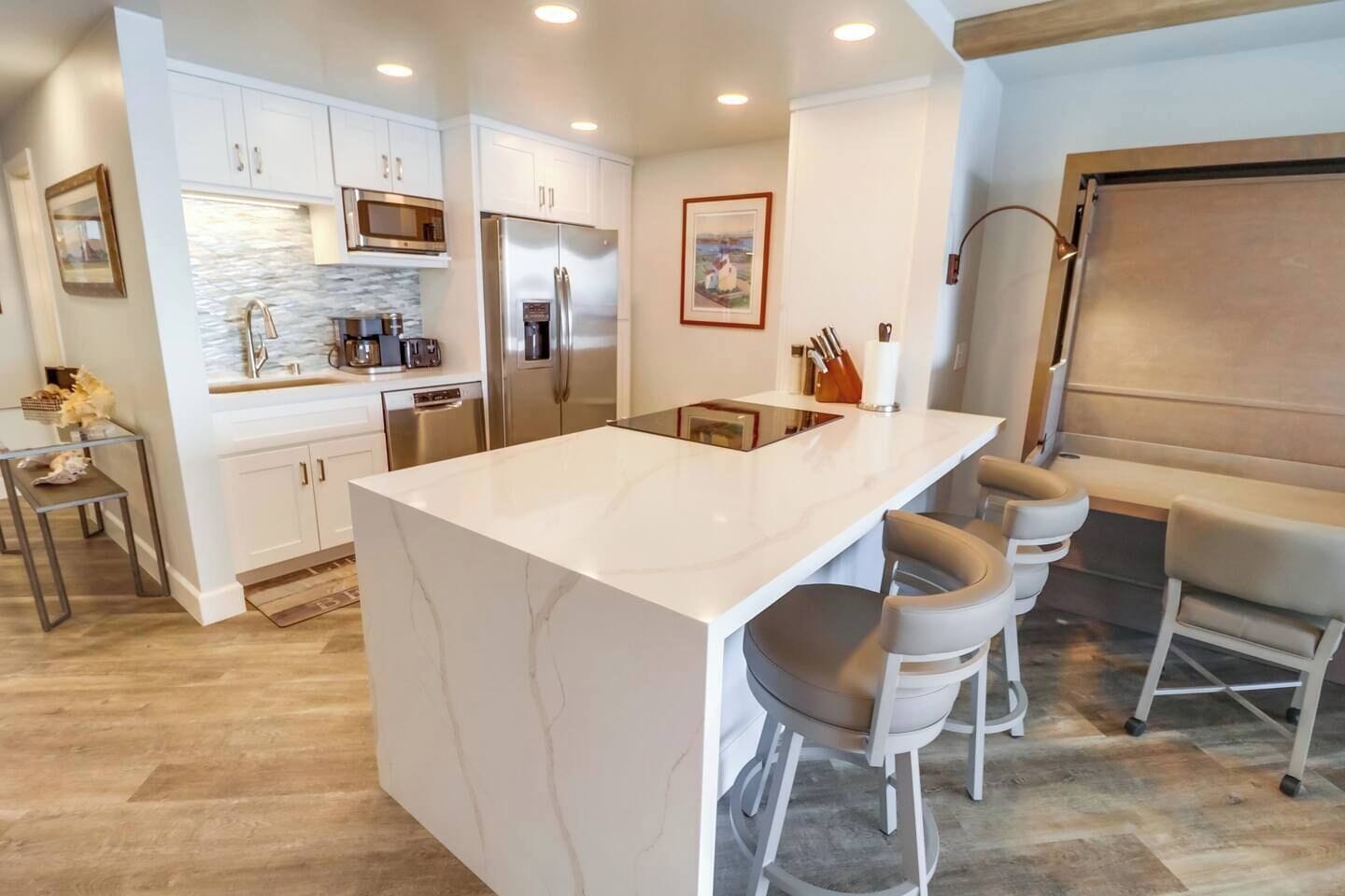 A modern kitchen with white cabinetry, a large island with bar stools, stainless steel appliances, and a tiled backsplash.