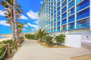 A modern hotel with a long, straight pathway leading to the entrance, surrounded by palm trees and a beach view. - Luxe Oceanfront view, murphy bed, parking and pool (San Diego)