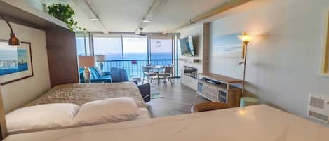 Habitación de hotel con cama, escritorio, televisor y balcón con vista al mar.
