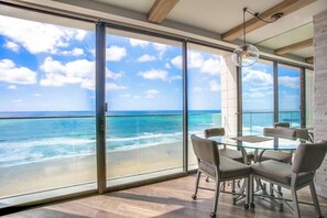 Une pièce avec une table et des chaises en verre, une vue sur l’océan et un ciel dégagé.