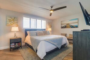 A bedroom with a bed, a nightstand, a bookshelf, a ceiling fan, and artwork on the walls.
