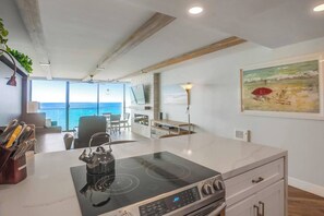 A modern kitchen with a large island, a kettle, and a view of the ocean.