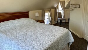 Une chambre à coucher avec un grand lit, une chaise, une table de chevet et une fenêtre avec des rideaux.