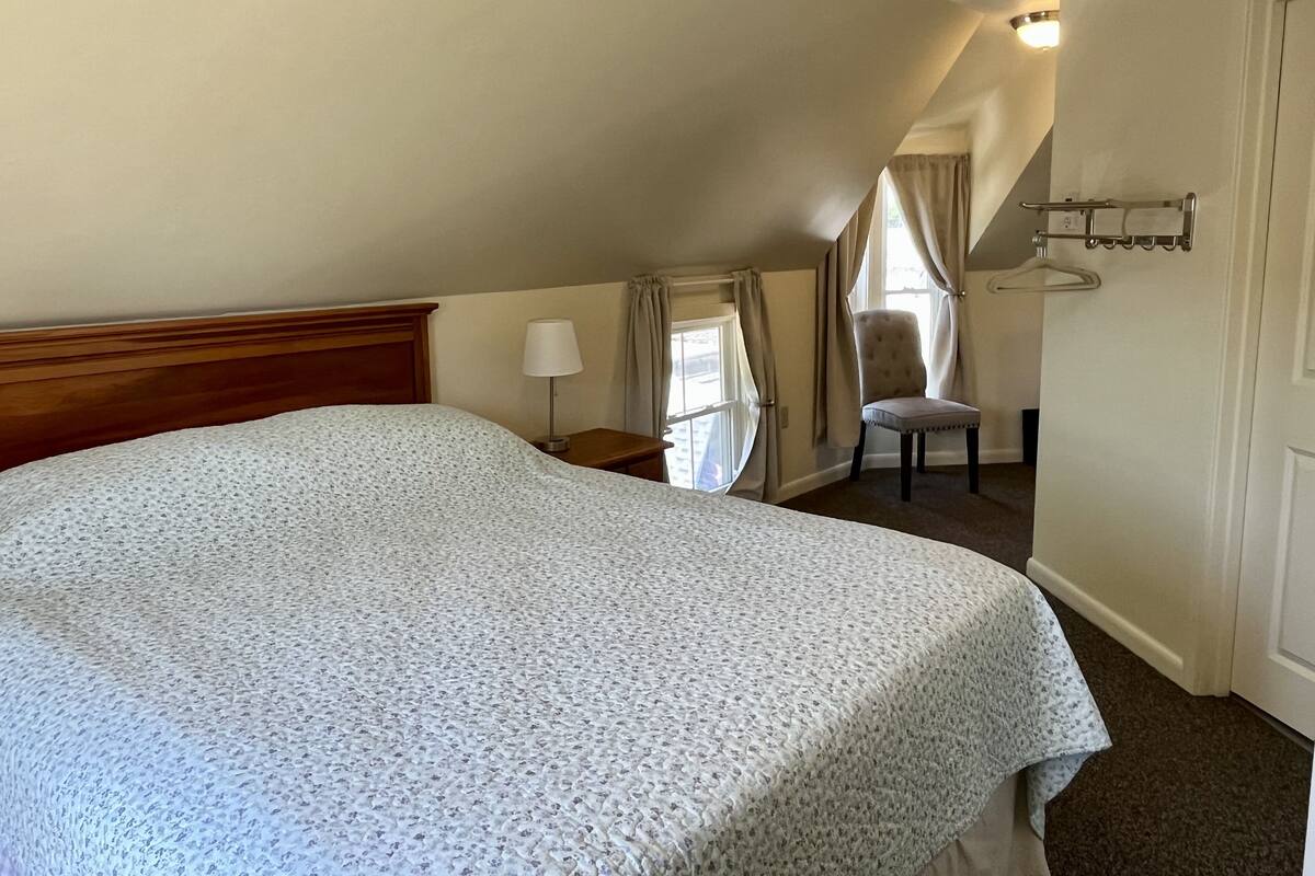 Ein Schlafzimmer mit einem großen Bett, einem Sessel, einem Nachttisch und einem Fenster mit Vorhängen.