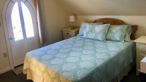Une chambre à coucher avec un lit, une table de chevet, une lampe, une fenêtre avec des rideaux et une porte.