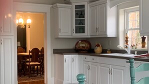 Een keuken met witte kasten, een eethoek met houten stoelen, en een raam met decoratieve accessoires.