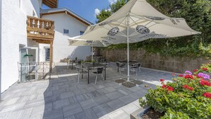 An outdoor patio with tables and chairs, umbrellas, and a stone wall. - HomeHotel Salzberg (Berchtesgaden)