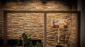 A room with a stone wall, a framed deer painting, a wooden table, and a plaid sofa. - HomeHotel Salzberg (Berchtesgaden)